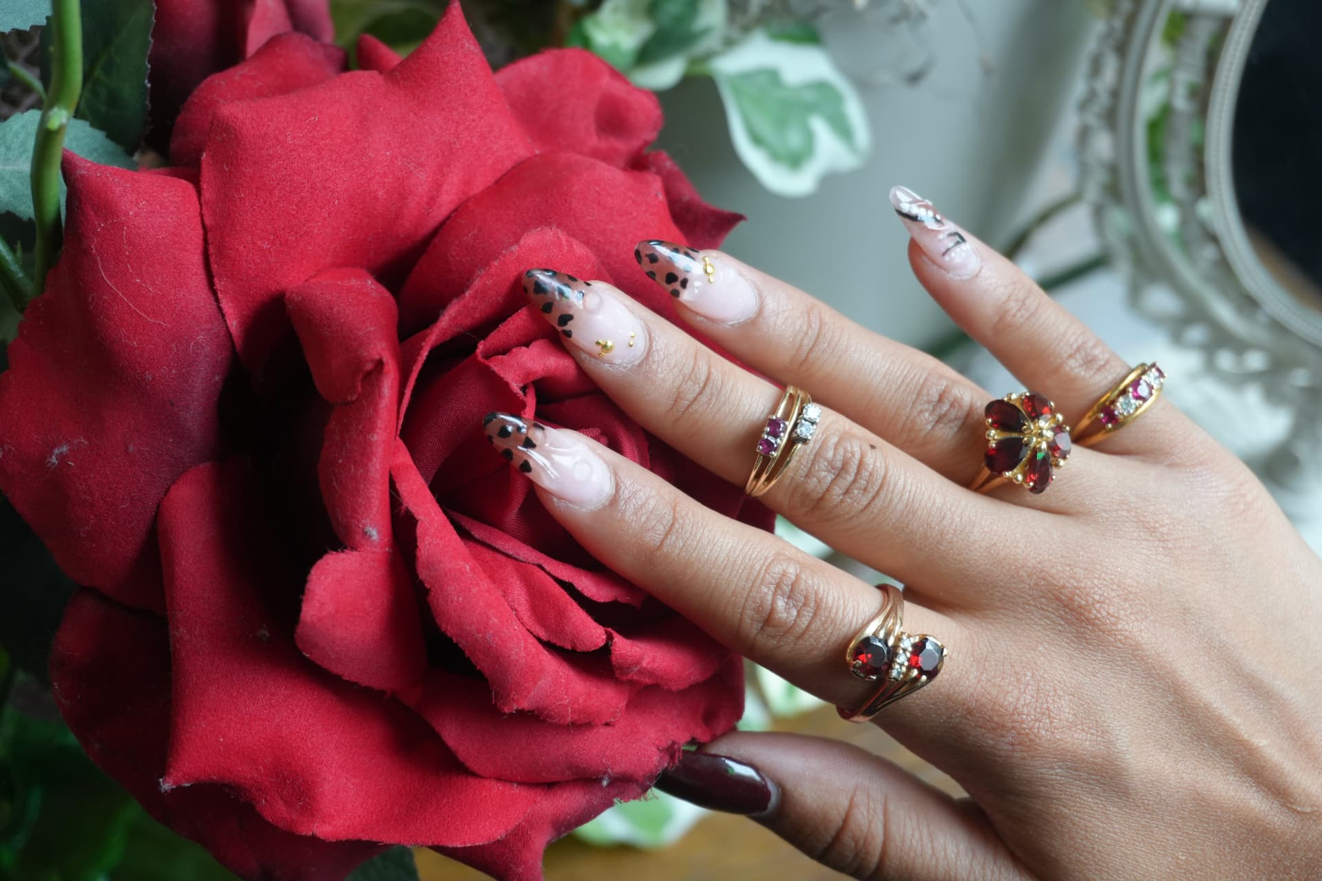 A hand wearing garnet, ruby and diamond gold rings resting on a red rose