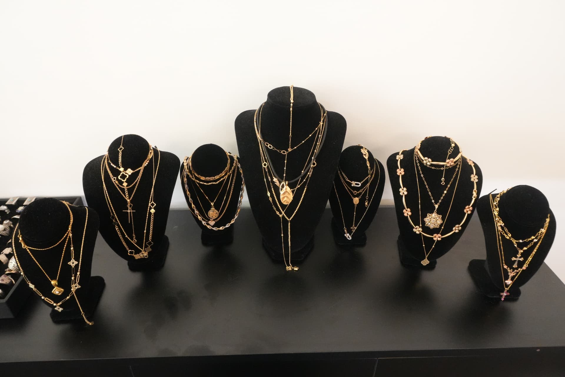 A row of black velvet busts displaying layered gold necklaces and pendants