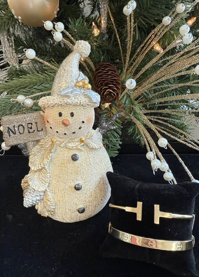 Gold bangles on a velvet pillow next to a Noel snowman
