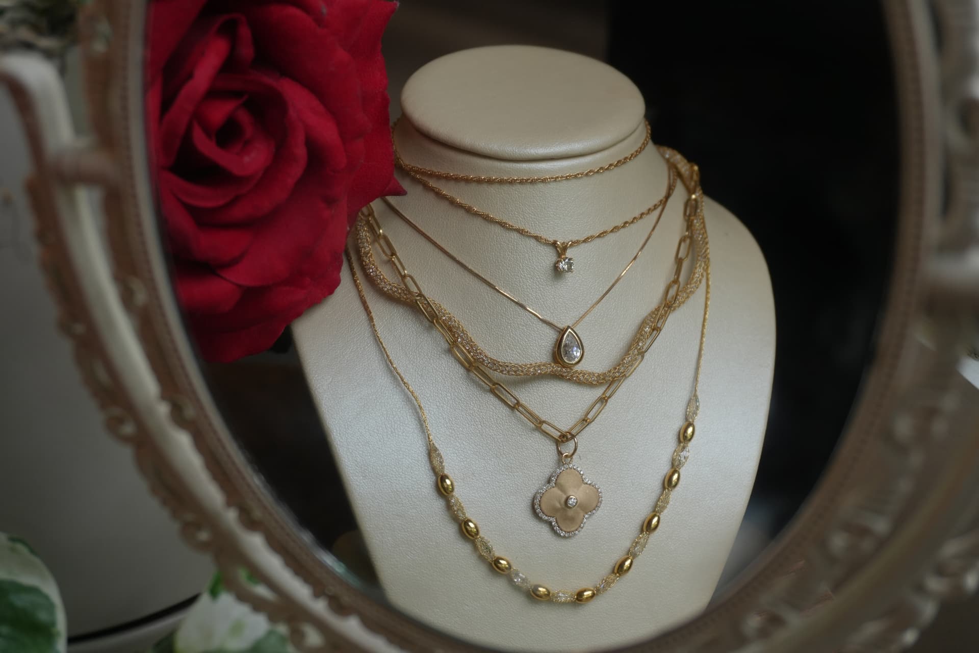 Layered gold necklaces with diamond and clover pendants reflected in an oval mirror