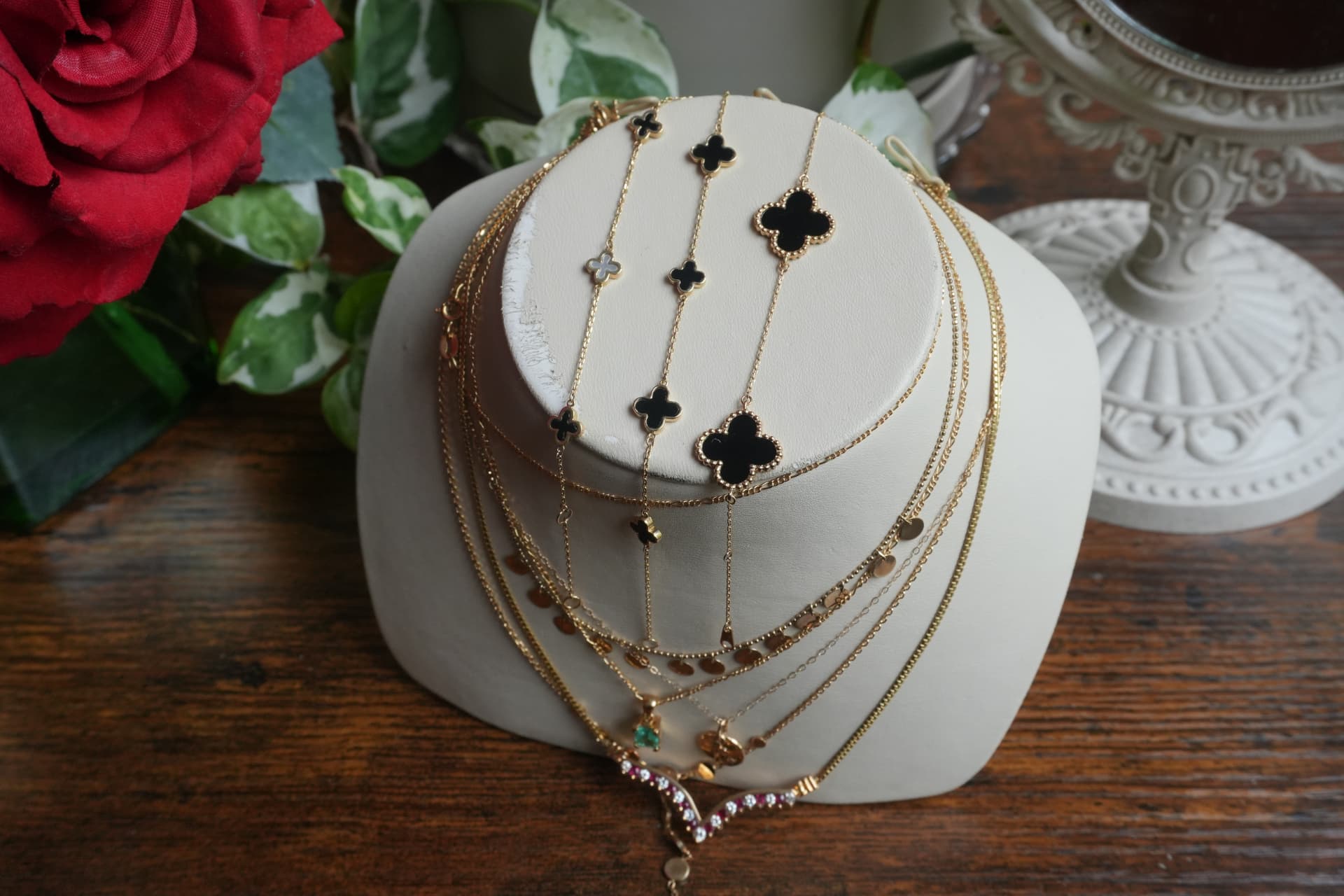 Gold and black onyx clover bracelets and layered chains on a cream bust